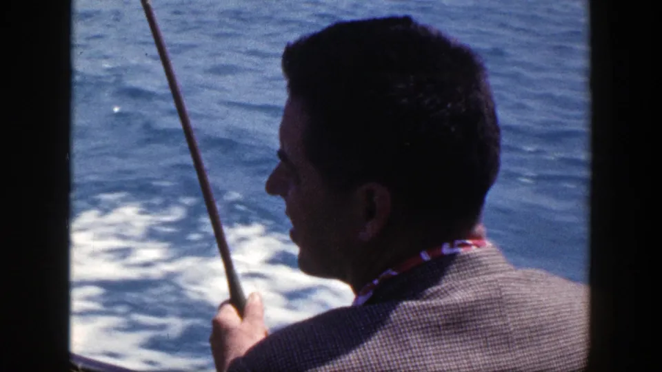 1948 New York 8mm frame showing an adult man in profile holding a fishing rod as water churns beside the boat.