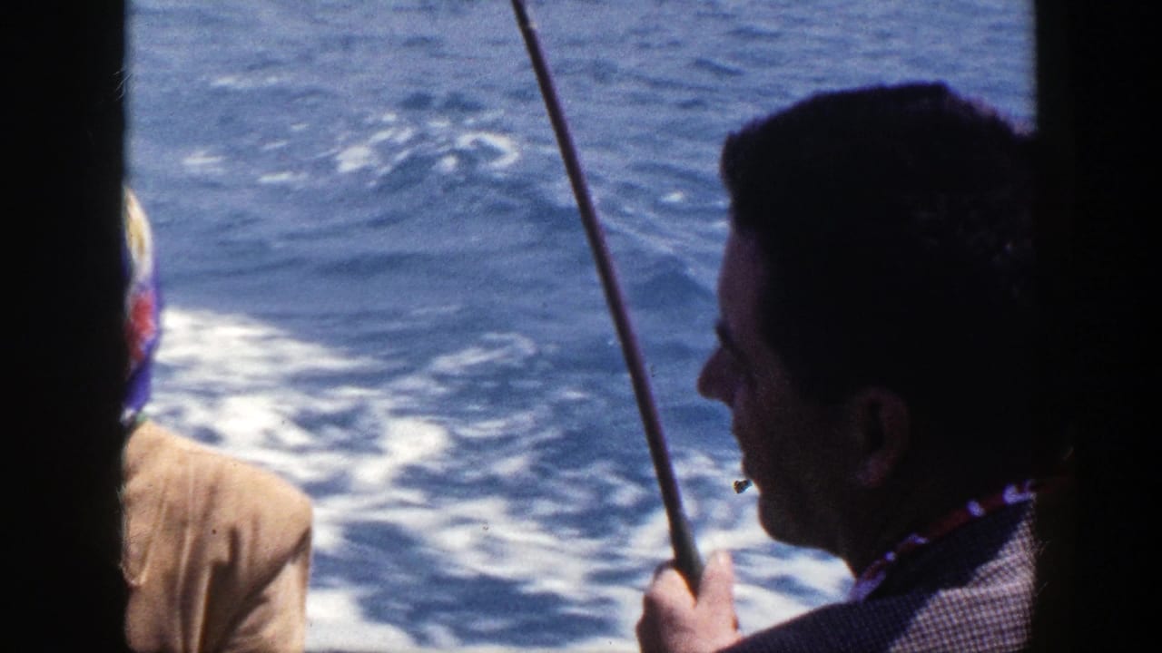 Adults on a moving boat with fishing rods and blue water behind them.