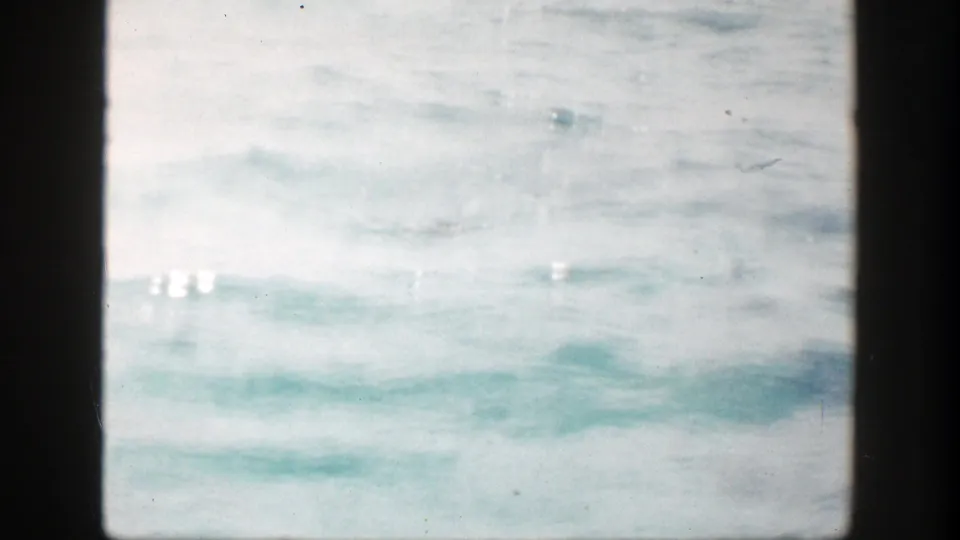 Soft 8mm frame of bright sea water and low wave texture, with no vessel, landmark, or person clearly identifiable.