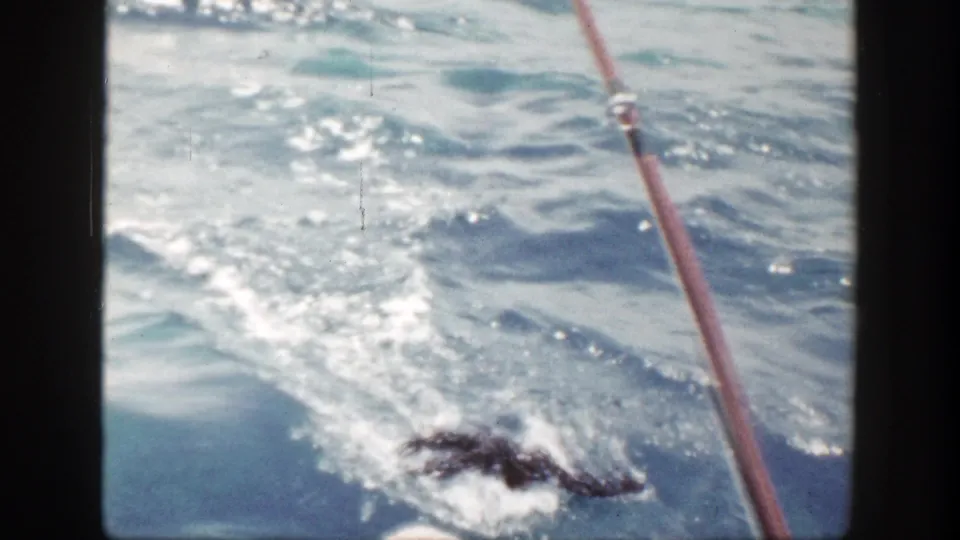 1948 New York 8mm frame showing a rod or pole at right and a fish splashing at the surface beside the boat.