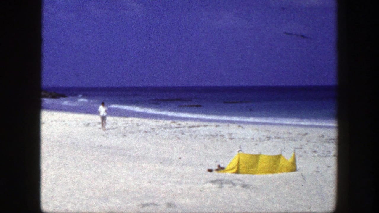Yellow tent on a white sand beach with distant people near the shoreline.