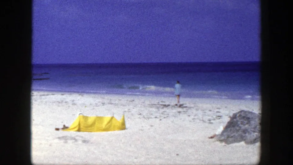 Final 1948 New York beach frame with a yellow tent, a distant shoreline figure, blue water, and a sand mound at right.