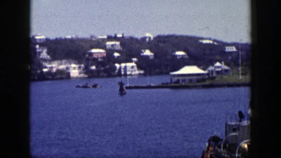 1948 New York coastal view from a boat, with small craft on the water and white buildings below a wooded hillside.