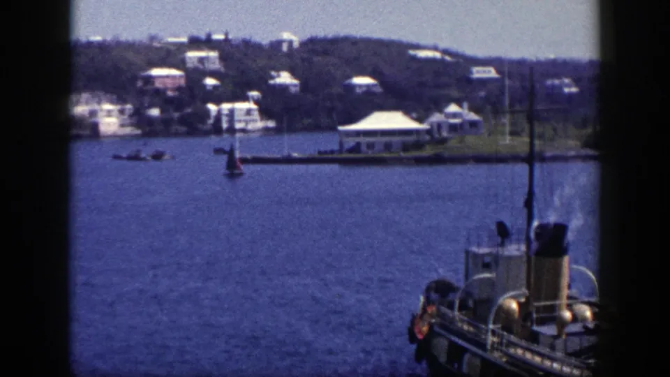 1948 8mm view of a steam boat on New York harbor water, with a small sailboat and hillside buildings in the distance.