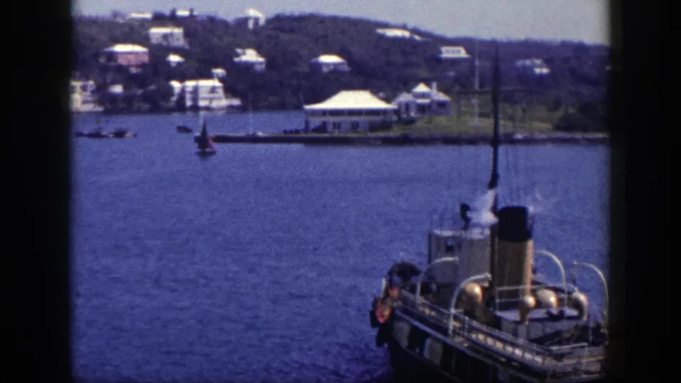 Soft 8mm harbor view from 1948 New York, with a steam boat at the edge of frame and a small sailboat near shoreline buildings.