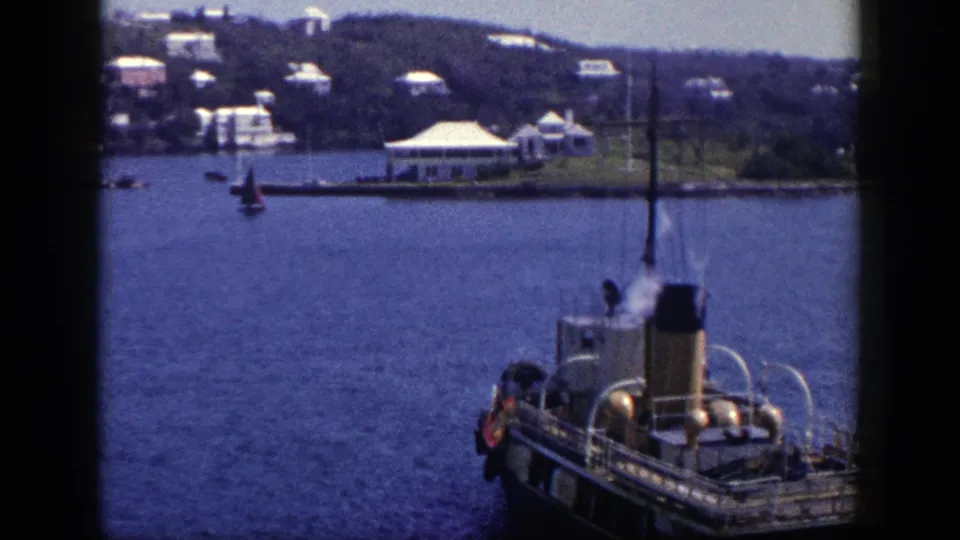 New York 1948 home-movie frame showing a steam boat in the foreground, faint steam, open water, and a distant settled shoreline.