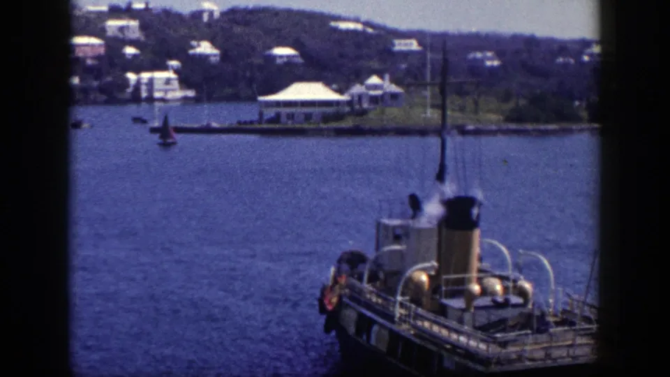 1948 New York 8mm frame showing a steam boat in harbor water, with a small sailboat and tree-lined shore in the distance.