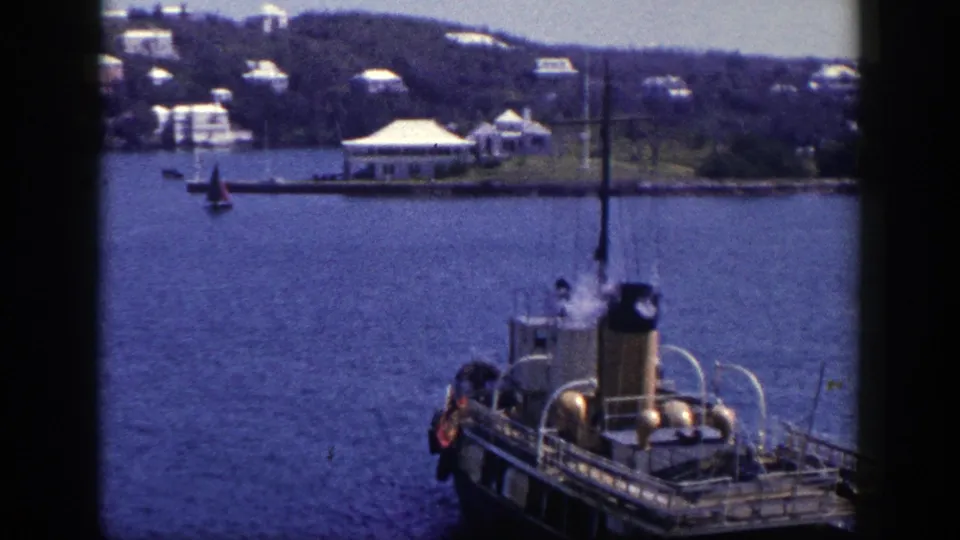 1948 New York harbor view with a steam boat in the foreground and a small sailboat near a low shoreline structure.