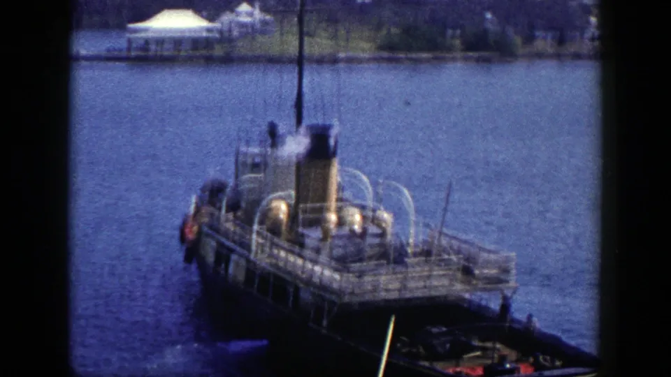 A soft, grainy 8mm frame shows the steamboat expelling steam while crossing blue water near the New York shoreline.