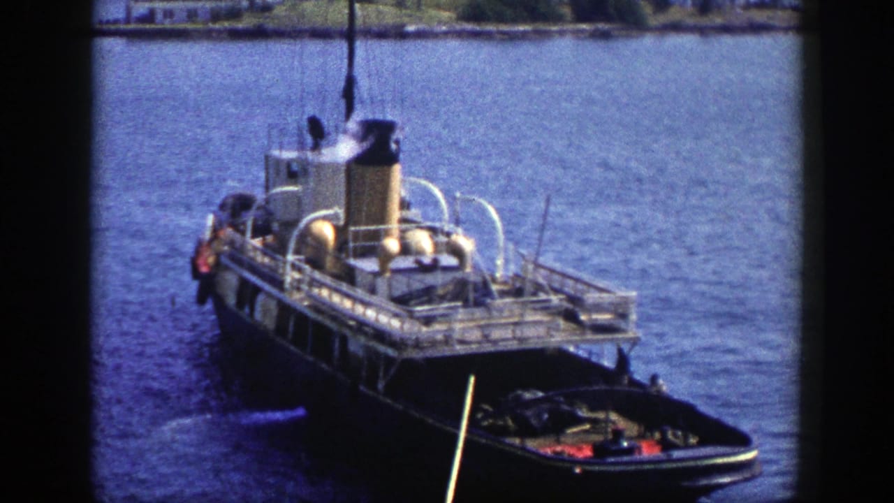 1948 New York home-movie frame showing a docked steam vessel with smoke above the stack and small craft near the stern.