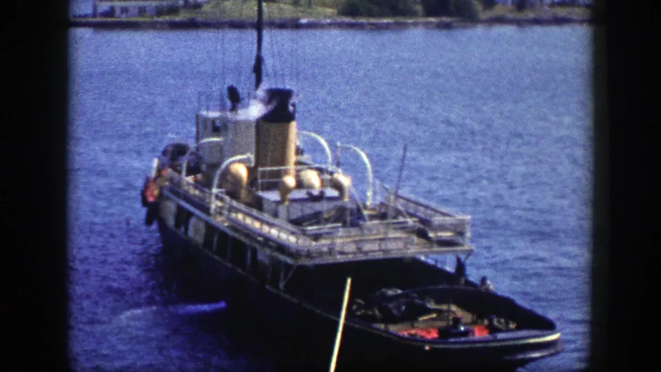 1948 New York home-movie frame showing a docked steam vessel with smoke above the stack and small craft near the stern.