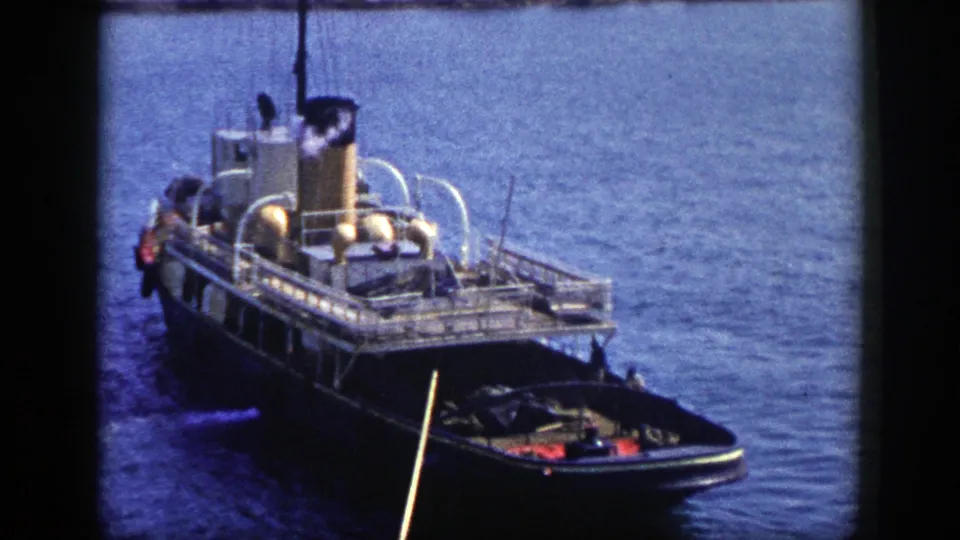 1948 New York home-movie view of the steam vessel's rail decks, stack, and stern-side small craft on calm harbor water.