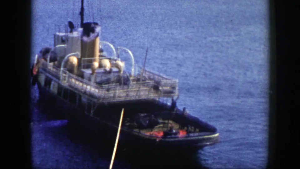 1948 New York frame showing the docked steam vessel from above, with a small boat near the stern and smoke rising into the harbor view.