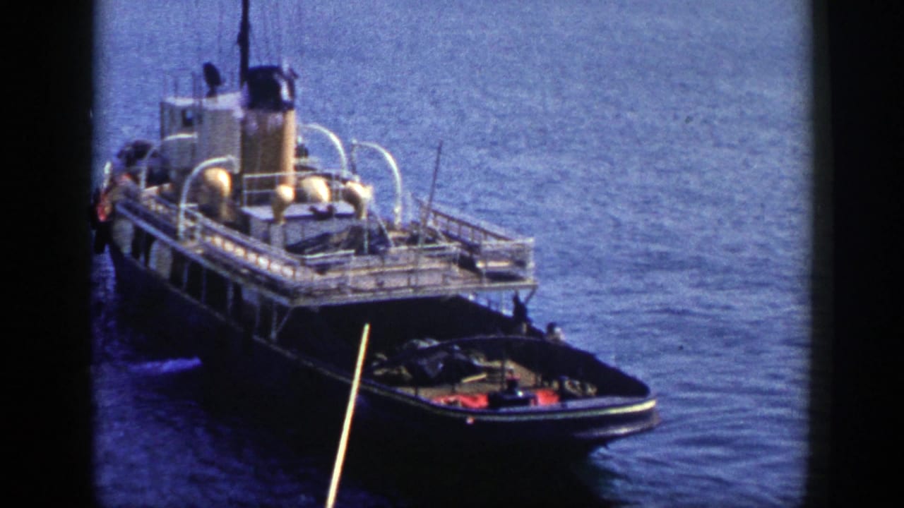 1948 New York 8mm frame showing a tugboat on blue water, smoke from the stack, white railings, and a small boat near its bow.