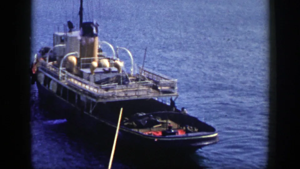 1948 New York 8mm frame showing a tugboat on blue water, smoke from the stack, white railings, and a small boat near its bow.