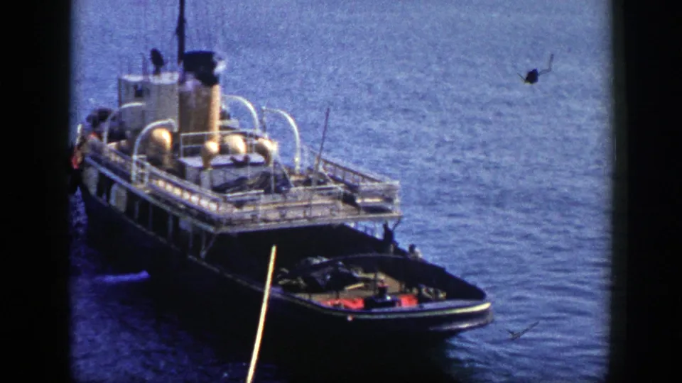 Elevated 1948 New York home-movie view of a tugboat, its smokestack releasing smoke while a small boat sits near the bow.