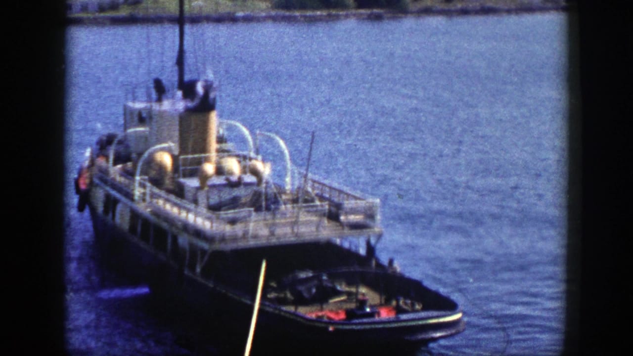 Dark-hulled steamboat beside calm blue water with dock gear visible.