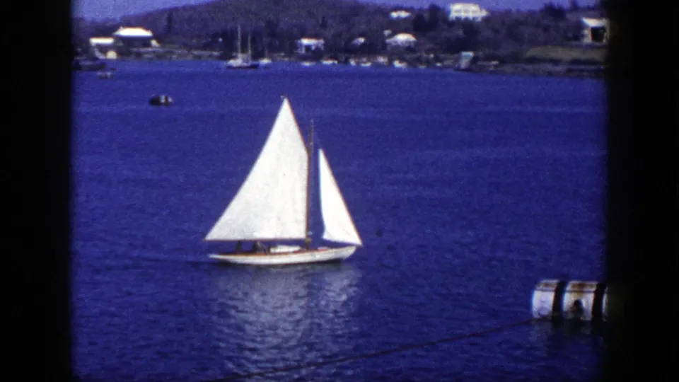 1948 New York 8mm frame showing a white sailboat under sail on calm blue water, with shoreline buildings in the background.