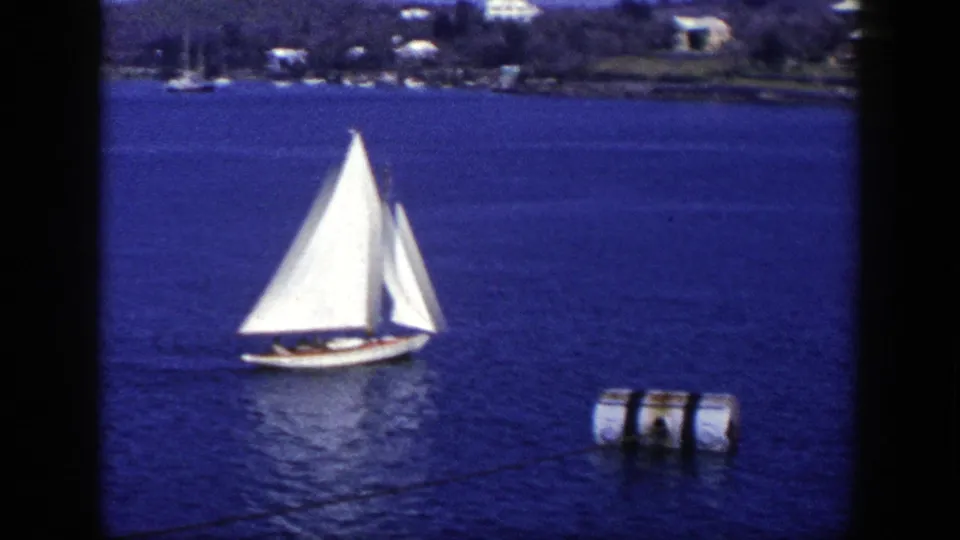 A white-sailed yacht continues across blue water in the 1948 New York home-movie scene, with a buoy in the foreground distance.