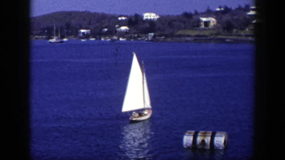 Final 1948 New York 8mm frame with the sailboat drifting right of center, a floating buoy nearby, and a wooded shoreline beyond.