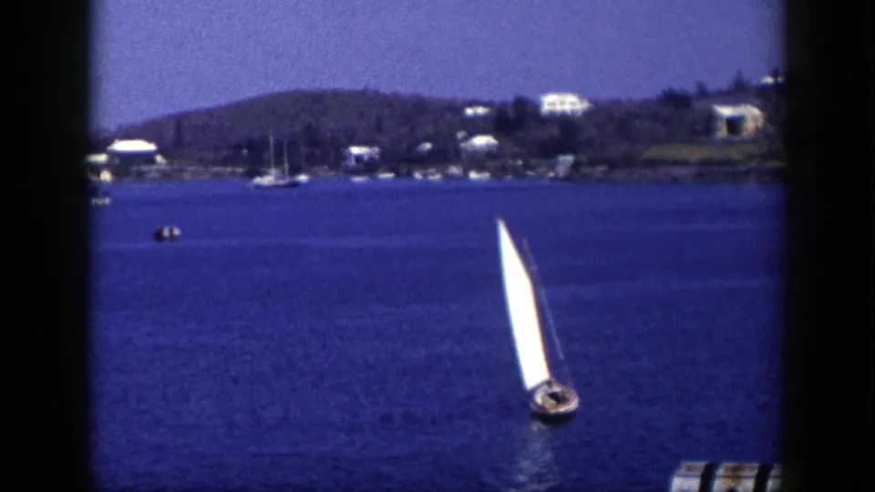 1948 New York 8mm frame with a sailboat near the lower center, a buoy at the edge, and a tree-lined shore with homes across the water.