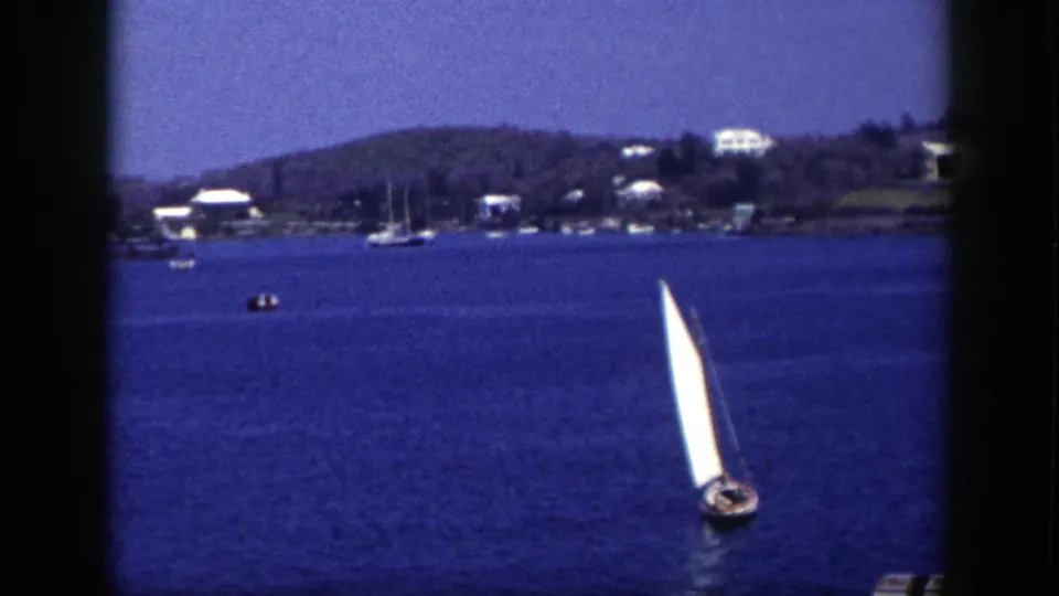 1948 New York 8mm frame showing a white sailboat on deep blue water near a distant shoreline with houses and low hills.