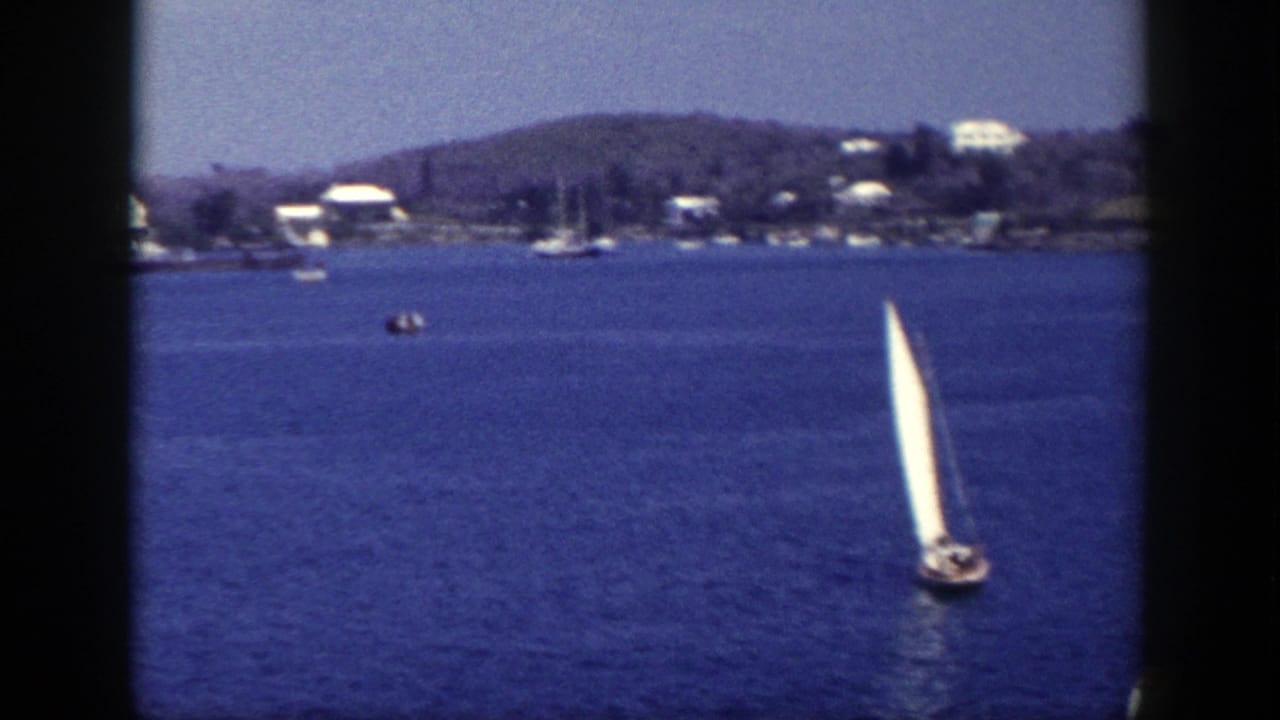 1948 New York 8mm frame showing sailboats on calm blue water with shoreline houses and low hills in the distance.