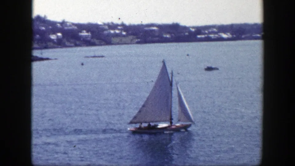 1948 New York 8mm frame of a white-sailed boat moving across blue harbor water, backed by a blurred shoreline.