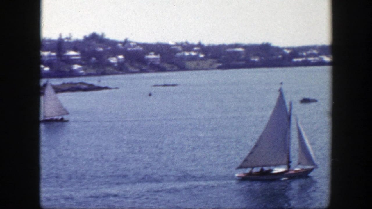 1948 New York home-movie frame of a sailboat on blue water with houses along the far shoreline.