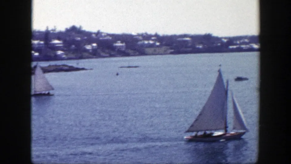 1948 New York home-movie frame of a sailboat on blue water with houses along the far shoreline.