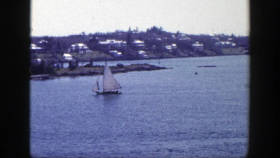 1948 New York 8mm frame showing a sailboat below a residential shoreline across the water.