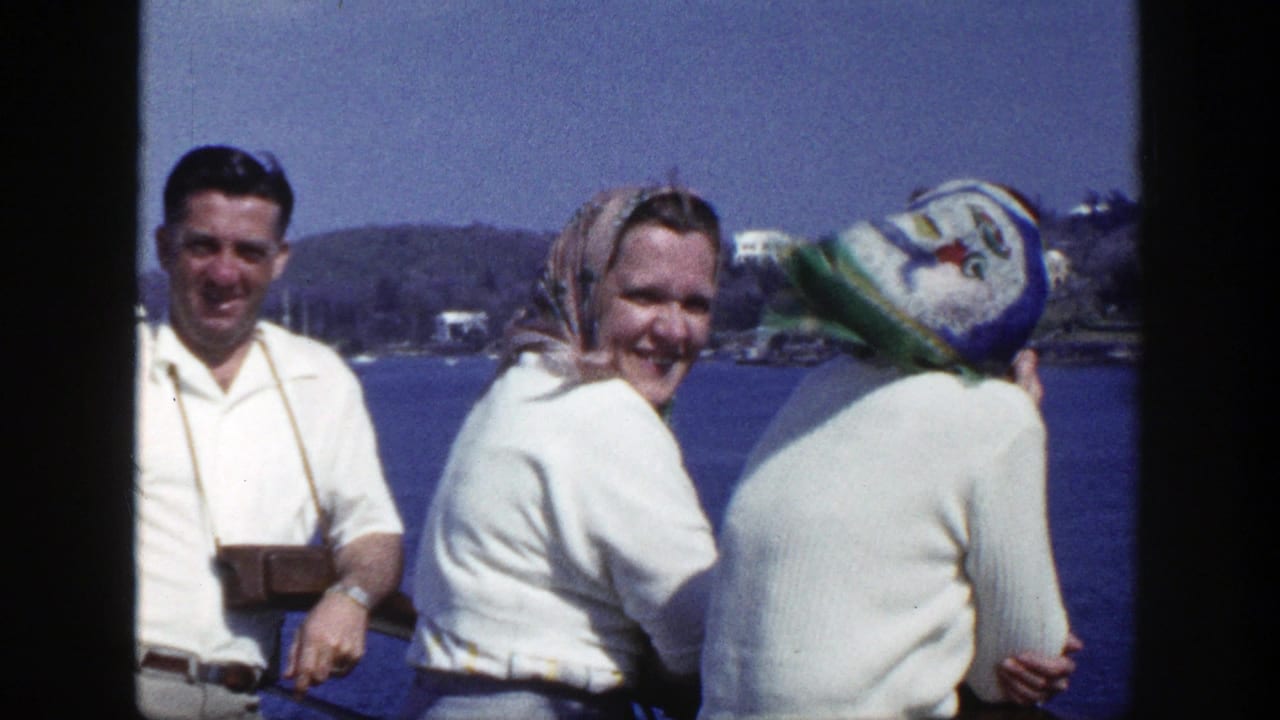 Three adults in white clothing stand by blue water, with a man wearing a camera around his neck.