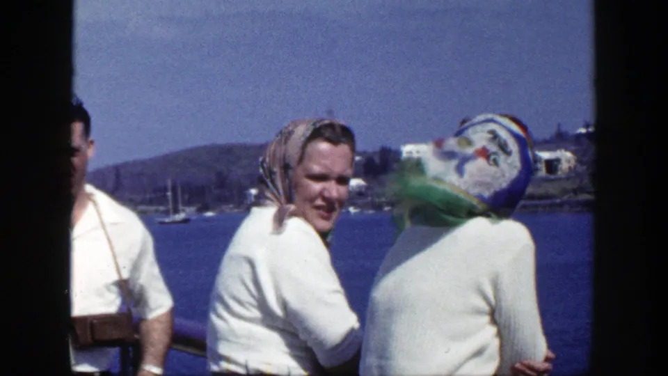 1948 New York home-movie frame of adults smiling and turning in wind near a lake, with a camera partly visible.