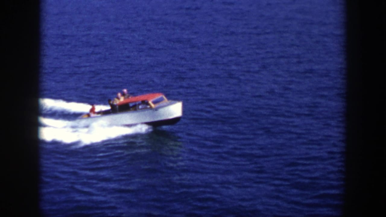 1948 New York home-movie frame showing a red and white motorboat moving across open blue water with passengers visible.