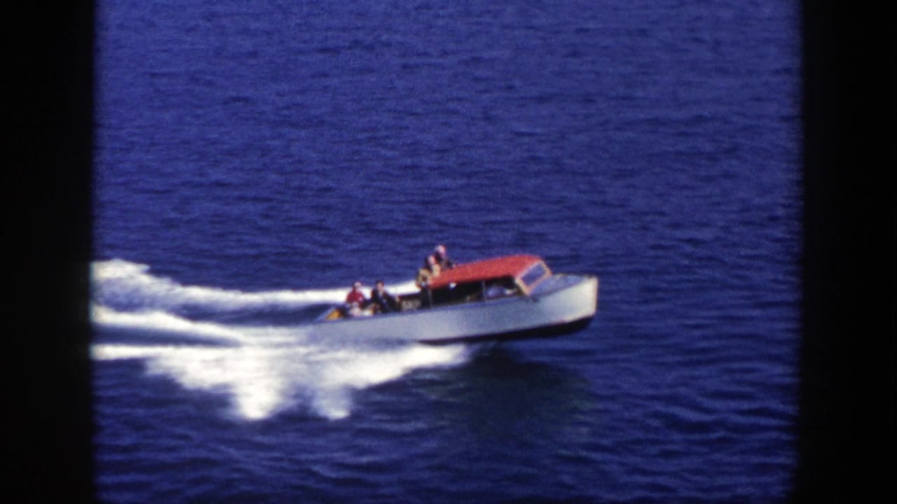1948 New York 8mm frame of a white motorboat with a red canopy moving across deep blue water with passengers visible.