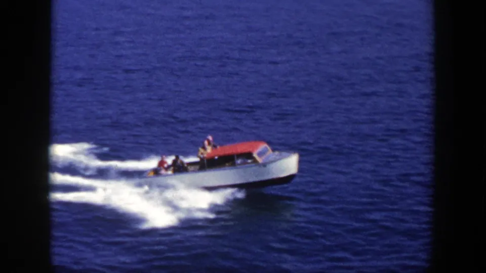 White recreational motorboat with a red canopy continues across New York water in the 1948 home-movie clip.