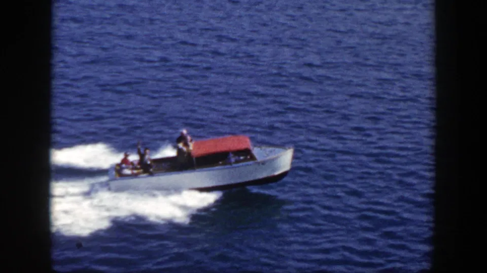 The 8mm frame shows a white motorboat with a red canopy and several passengers riding over blue water in New York.