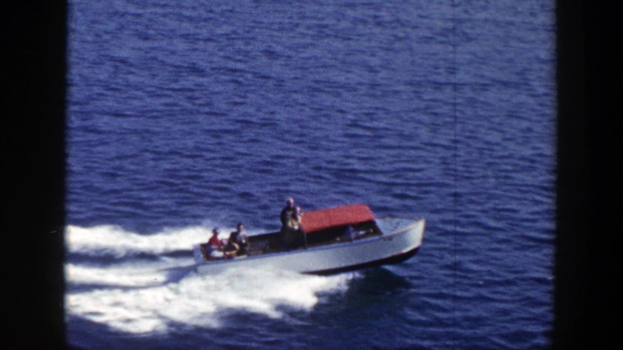 Small white motorboat with a red canopy speeding across blue water.