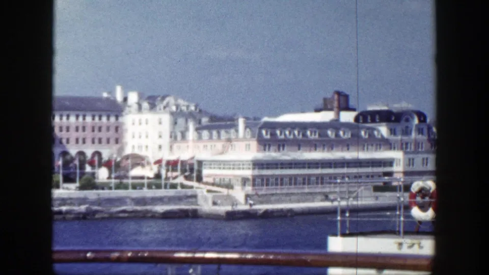 1948 New York home-movie frame of a large waterfront building seen past a boat rail and blue water.