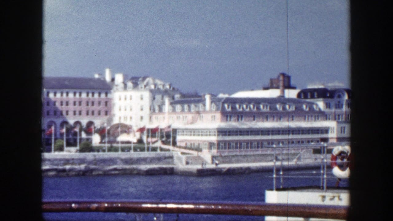 Waterfront buildings seen across blue harbor water from a moving ship.