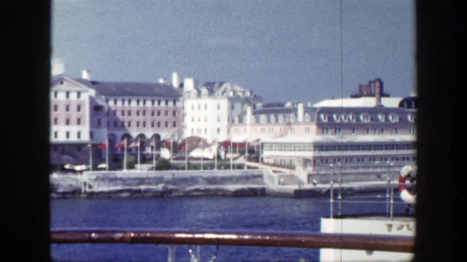 1948 New York harbor view showing waterfront facades, arched openings, flags, and a foreground ship rail.