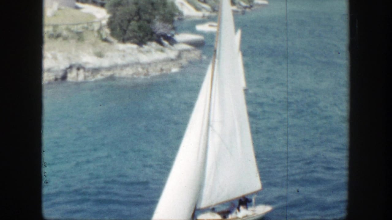 White sailboat passing near a rocky shoreline on blue water.