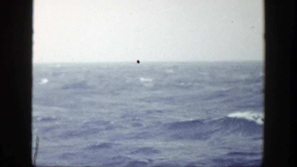 Rolling ocean water stretches toward a faint horizon, with visible 8mm grain and small dust specks.