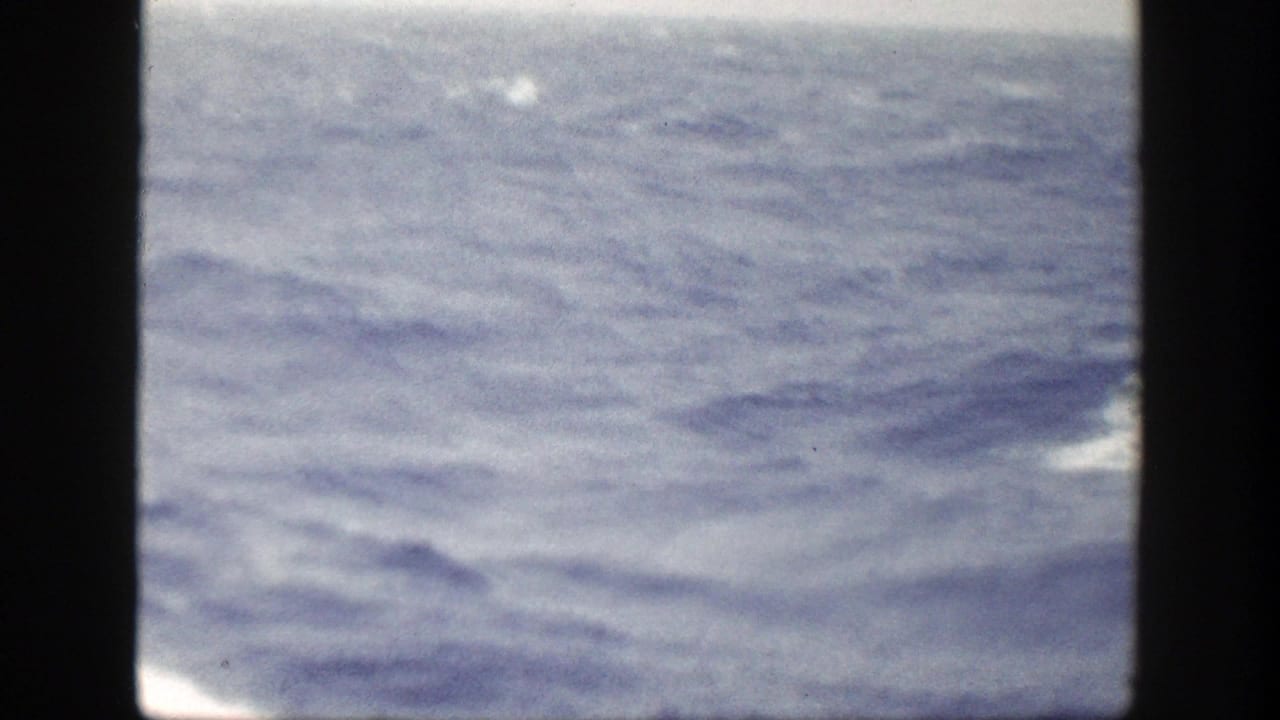 Choppy ocean seen past dark film borders with part of the ship bow at the lower right.