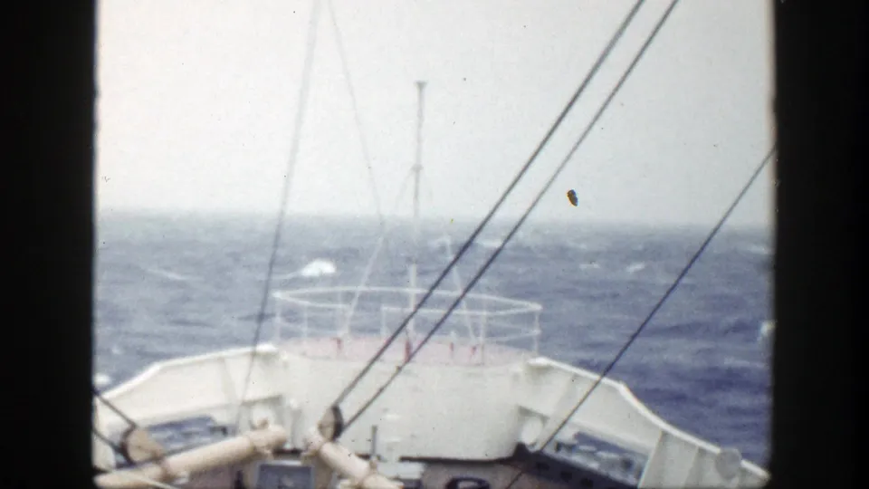 1948 8mm shipboard frame showing the bow, railings, mast, and rigging as the vessel moves through rough seas.