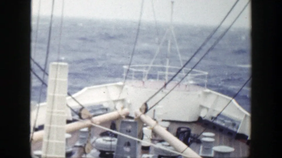 1948 8mm frame showing more of the vessel deck, with railings, a mast or post, rigging, and rough water ahead.