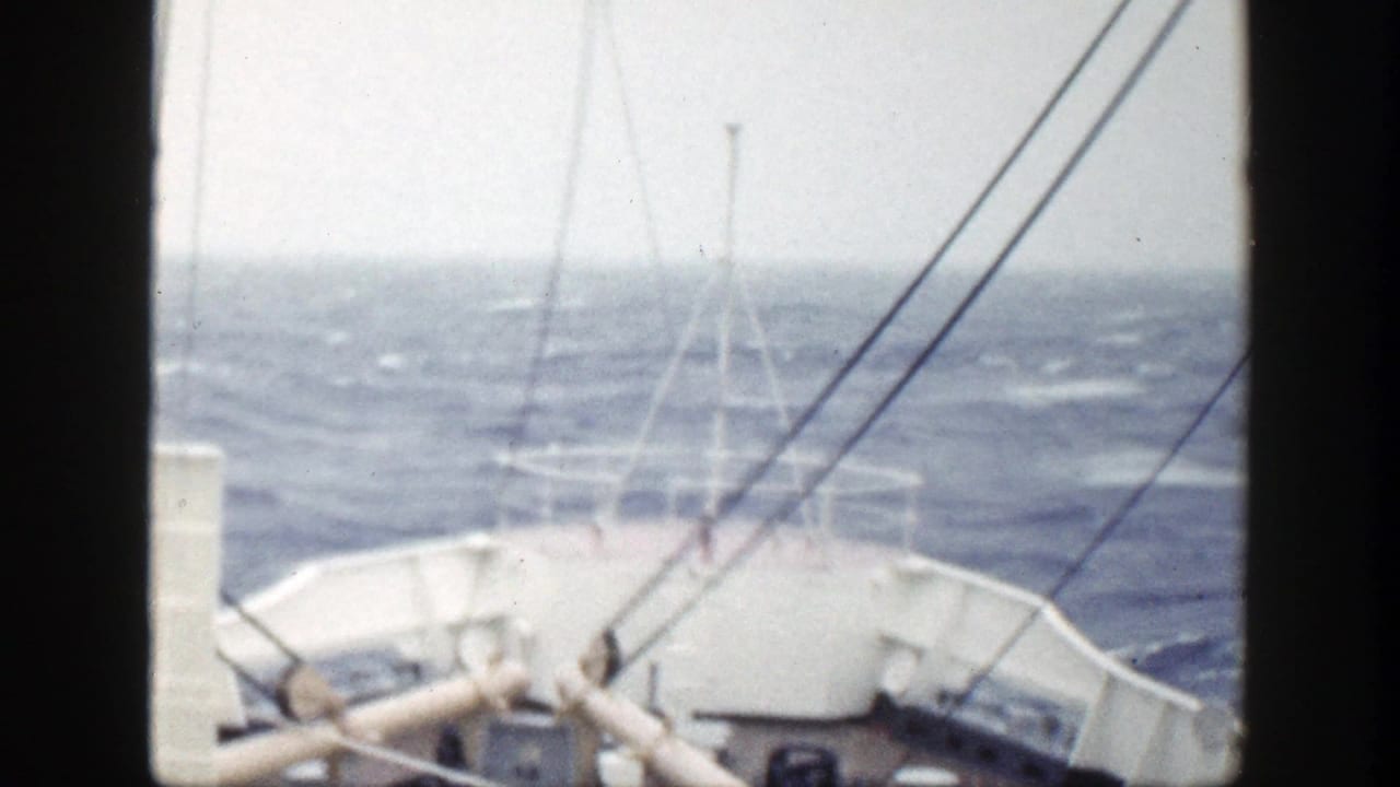 Ship bow and railings face choppy open water with rigging lines in view.