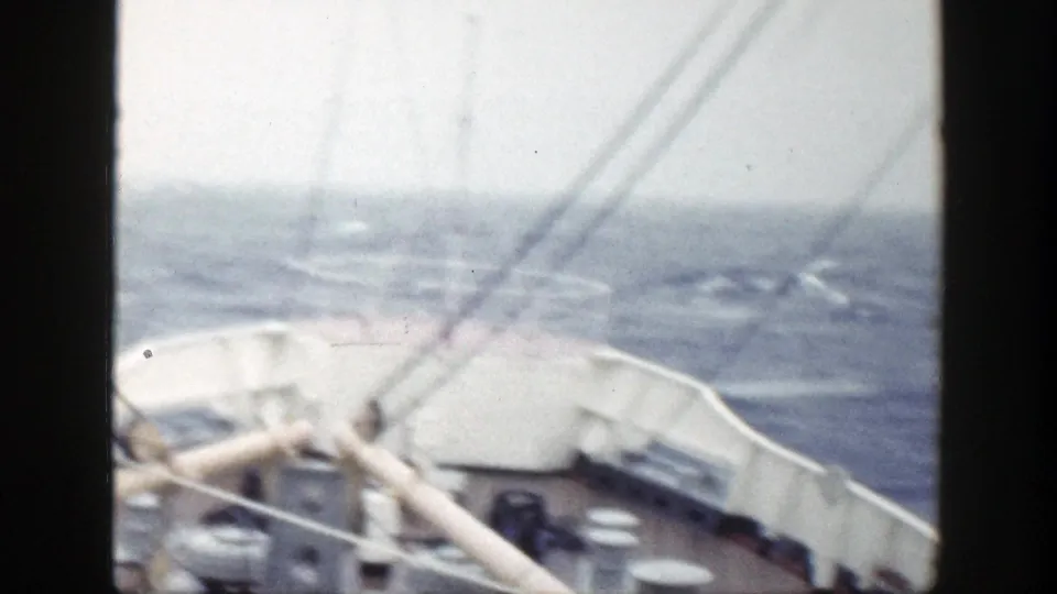 Shipboard deck view with pale railings and diagonal rigging lines over rough water in 1948 8mm footage.