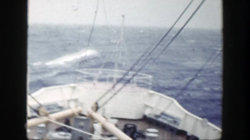 The bow and deck railings remain in view as rough sea and whitecaps pass beneath an overcast sky.