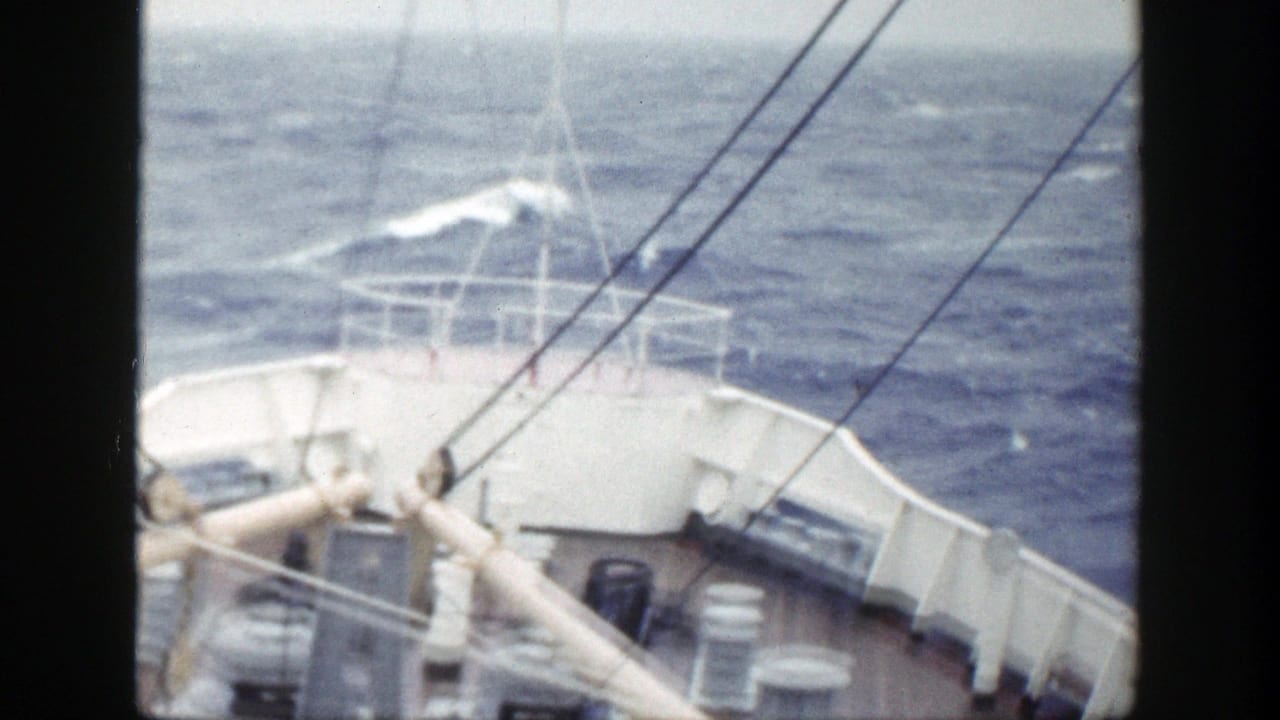 Ship bow and railings seen over choppy blue ocean with whitecaps.